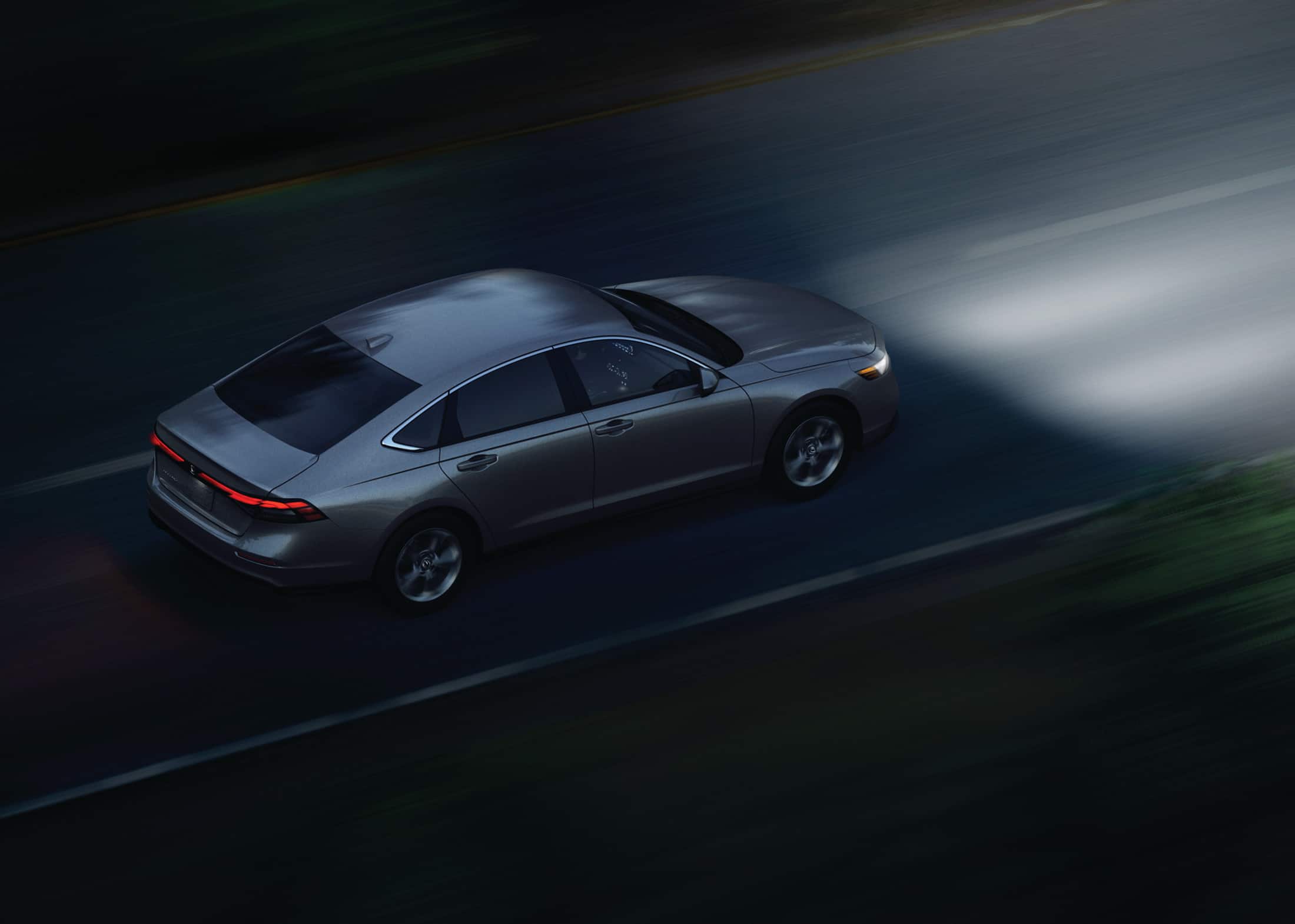 High-angled 3/4 rear passenger-side shot of the 2023 Honda Accord LX in Solar Silver Metallic, shown driving on an open road at night.