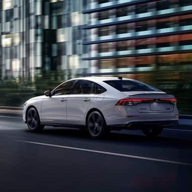 2026 Honda Accord 3/4 rear view in Platinum White Pearl driving in the city at night.