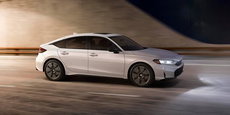 2027 Honda Civic Hatchback Touring Hybrid in Platinum White Pearl profile driving through a tunnel (Compact Hatchback).